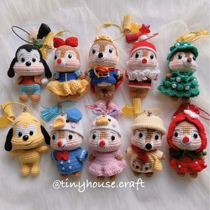 May include: A collection of ten crocheted plush toys, including a dog, a squirrel, and a chipmunk, dressed in various outfits. The toys are all wearing keychains and are arranged in two rows on a white fabric background. The text "@tinyhouse.craft" is visible at the bottom of the image.