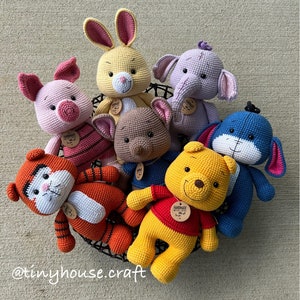 May include: A collection of seven crocheted stuffed animals, including a pig, rabbit, elephant, bear, tiger, and two bears. The animals are all different colors and have different facial expressions. The animals are sitting in a black wire basket. The text "HANDMADE WITH LOVE" is on a tag attached to one of the bears.
