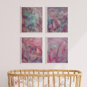 May include: Four abstract paintings in white frames, each featuring a swirling, colorful design in shades of pink, purple, and blue. The paintings are hung on a white wall above a wooden crib.