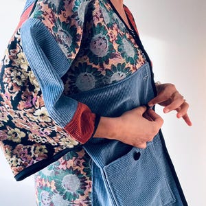 May include: A patchwork jacket with a floral pattern and blue corduroy panels. The jacket features a black trim, a button closure, and a pocket. The sleeves have a red accent.