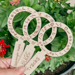 May include: Three wooden nature scavenger hunt tools with magnifying glass rings. The rings are labeled with different animals, insects, and plants. The tools are labeled "Scavenger Hunt", "Bugs", and "Tracks".