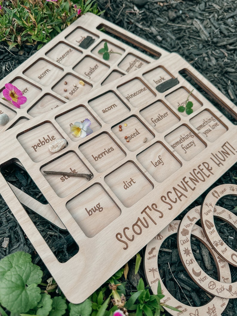 May include: Wooden nature scavenger hunt game with a set of rings. The game board has slots for finding items like acorns, pinecones, feathers, leaves, and bugs. The rings have images of nature items like a sun, moon, cloud, and a deer.