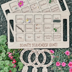 May include: Wooden game board with a brown stain and rounded edges. The board is divided into 16 squares with text and images in each square. The text includes words like "acorn", "pinecone", "feather", "berries", "seed", "something fuzzy", and "something you love". The board is labeled "Scout's Scavenger Hunt!" and has three magnifying glass shapes with the words "Bugs", "Scavenger Hunt", and "Tracks" on them.