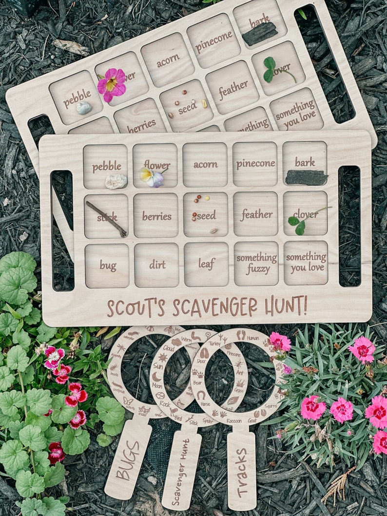 May include: Wooden game board with a brown stain and rounded edges. The board is divided into 16 squares with text and images in each square. The text includes words like "acorn", "pinecone", "feather", "berries", "seed", "something fuzzy", and "something you love". The board is labeled "Scout's Scavenger Hunt!" and has three magnifying glass shapes with the words "Bugs", "Scavenger Hunt", and "Tracks" on them.