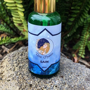 May include: A green glass bottle with a gold cap and a blue and white label. The label features a woman with a crown of stars and the text "Tree Mystic" and "SAIN". The bottle contains 50 ml of liquid.