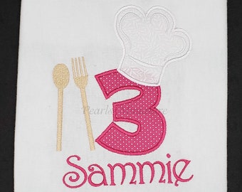 May include: White embroidered shirt with a pink number 3, a white chef's hat, and a gold spoon and fork. The name "Sammie" is embroidered below the number.