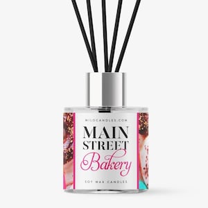 May include: A clear glass diffuser bottle with a silver lid and black diffuser sticks. The label is white with pink text that reads "Main Street Bakery" and "Soy Wax Candles" and a colourful image of a bakery item.