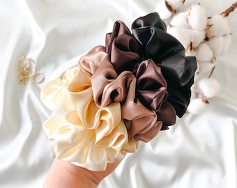 May include: Set of four satin scrunchies in shades of brown, beige, and cream. The scrunchies are arranged in a flower shape.