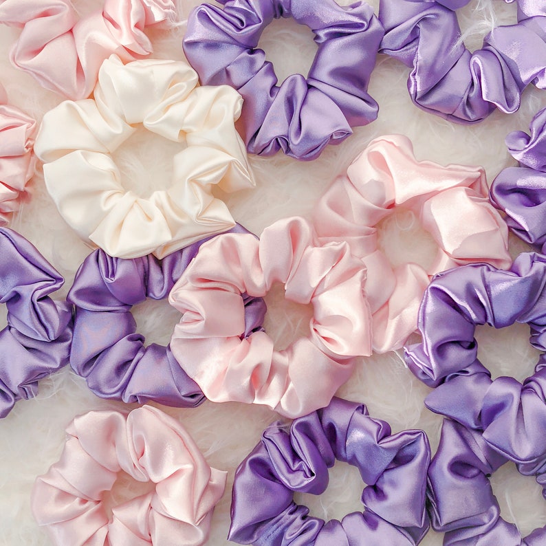 May include: A collection of colorful satin scrunchies in shades of pink and purple. The scrunchies are made of soft, silky fabric and are perfect for holding hair in place.