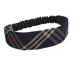 May include: A navy blue headband featuring a beige and red plaid design. The elasticated section is black. This hair accessory offers a classic look and is suitable for various hairstyles.