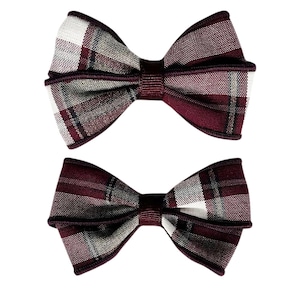 May include: Two bow ties featuring a plaid pattern in shades of deep burgundy, white, and grey. Each bow tie has a central knot made of solid burgundy fabric and finished edges in the same dark red tone, creating a structured, layered appearance.