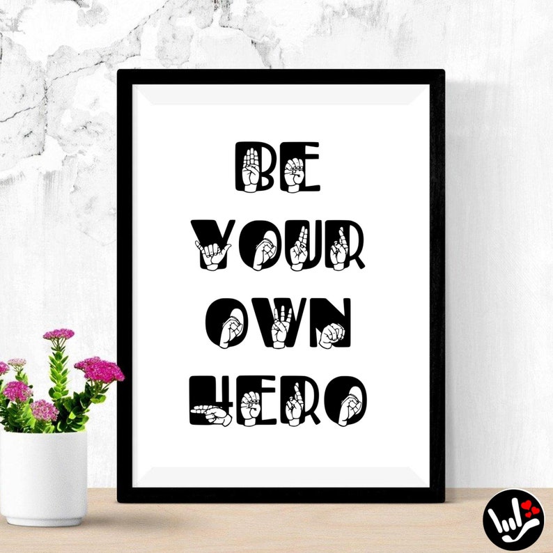 May include: Black and white print with the text "BE YOUR OWN HERO" in sign language. The print is framed in a black frame and is hanging on a white wall.