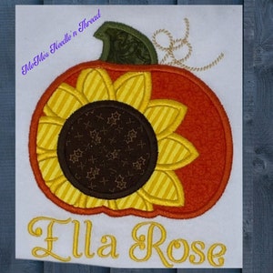 Puede incluir: Una tela blanca con una calabaza bordada con un dise&ntilde;o de girasol. La calabaza es naranja y amarilla con un tallo verde. El girasol tiene un centro marr&oacute;n y p&eacute;talos amarillos. El texto "Ella Rose" est&aacute; bordado debajo de la calabaza.