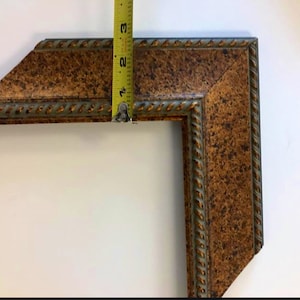 May include: A close-up of a corner of a picture frame with a rope-like design. The frame is made of wood with a brown and green finish. The frame is 2 inches wide.