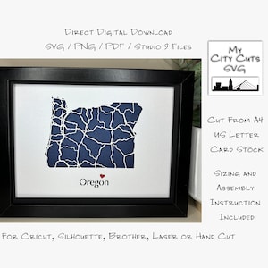 May include: A white paper cutout of the state of Oregon with blue rivers and a red heart in the centre. The cutout is framed in black and the text "Oregon" is below the cutout. The text "CUT FROM A4 US LETTER CARD STOCK" is on the right side of the image. The text "SIZING AND ASSEMBLY INSTRUCTION INCLUDED" is below the text "CUT FROM A4 US LETTER CARD STOCK". The text "FOR CRICUT, SILHOUETTE, BROTHER, LASER OR HAND CUT" is at the bottom of the image.