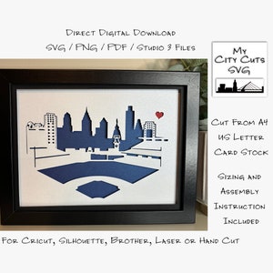 May include: A framed paper craft of the Philadelphia skyline with a red heart. The skyline is cut out of white cardstock and layered on a blue background. The text "CUT FROM A4 US LETTER CARD STOCK" is written in black ink on a white background. The text "SIZING AND ASSEMBLY INSTRUCTION INCLUDED" is written in black ink on a white background. The text "FOR CRICUT, SILHOUETTE, BROTHER, LASER OR HAND CUT" is written in black ink on a white background.
