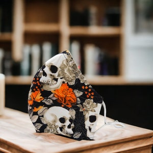 May include: A black face mask with a skull and floral pattern. The mask has orange flowers, white skulls, and a black background.