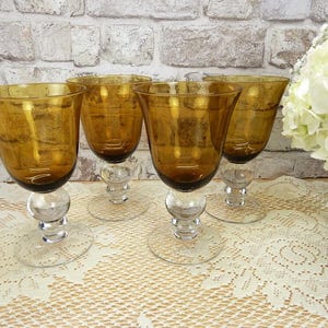 May include: A set of four amber-colored glass goblets with a textured, bubbled finish on the bowls. Each goblet features a clear glass stem with a prominent spherical node and a circular clear glass base, arranged in a group on a surface.