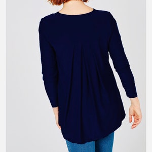 Puede incluir: Una camisa azul marino de manga larga con un corte holgado y un detalle de pliegues en la espalda.