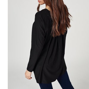 May include: A black long-sleeve top with a relaxed fit. The top has a V-neck and a slightly curved hemline. The sleeves are long and the fabric appears to be a soft, lightweight material. The top is shown from the side.