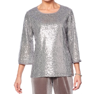 Può includere: Top argentato con paillettes, maniche a tre quarti e scollatura rotonda. La parte superiore è interamente ricoperta di paillettes scintillanti, creando un look glamour. Le maniche e lo scollo sono rifiniti con tessuto grigio. Il top è abbinato a pantaloni di velluto grigi coordinati.