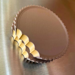 May include: A stack of round, metallic-looking cake boards with a scalloped edge. The boards are a light brown color with a textured surface. The edges are a lighter, cream color.