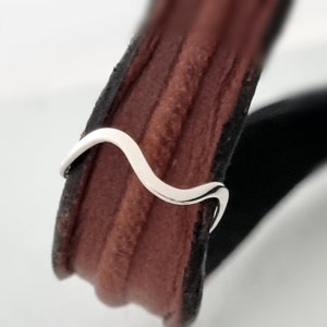Könnte beinhalten: Ein silberner, wellenförmiger Ring auf einem braunen Lederband.