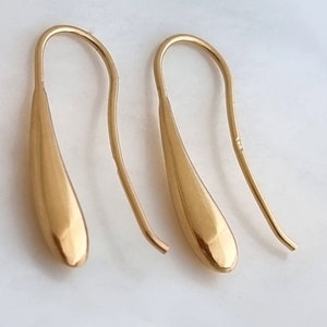 Op de afbeelding: Een paar gouden oorhangers in druppelvorm met een eenvoudige haaksluiting.