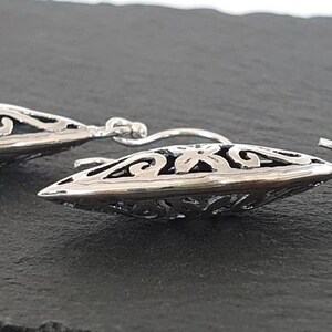 May include: A pair of silver dangle earrings with a delicate, intricate design. The earrings are shaped like a teardrop and feature a floral pattern.