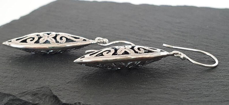 May include: A pair of silver dangle earrings with a delicate, intricate design. The earrings are shaped like a teardrop and feature a floral pattern.