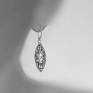 May include: A silver filigree earring with a teardrop shape. The earring is hanging from a person's ear.