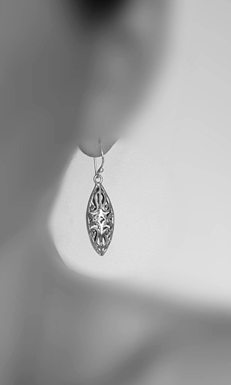 May include: A silver filigree earring with a teardrop shape. The earring is hanging from a person's ear.