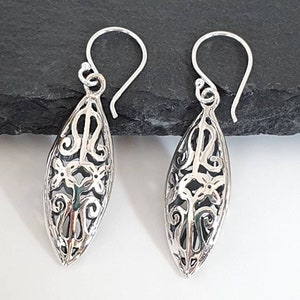 May include: A pair of silver dangle earrings with a delicate, intricate design. The earrings are oval-shaped and feature a floral pattern.