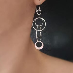 Op de afbeelding: Zilveren oorhangers met meerdere met elkaar verbonden cirkels. De onderste cirkel heeft een roze tint.