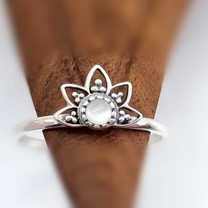 Pode incluir: Um anel de prata com uma pedra de madrepérola branca engastada em um design floral.