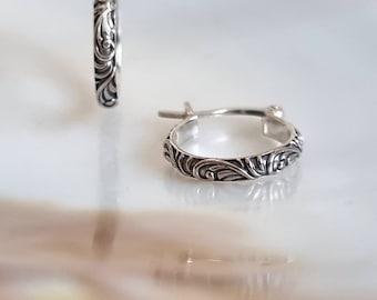 May include: A pair of silver hoop earrings with an intricate floral design. The earrings are small and delicate, and they would make a great gift for a special occasion.