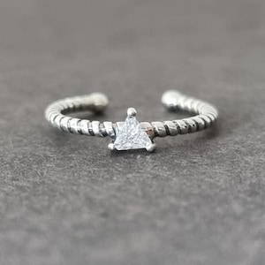 Può includere: Un anello d'argento con una fascia attorcigliata e una piccola pietra triangolare trasparente al centro.