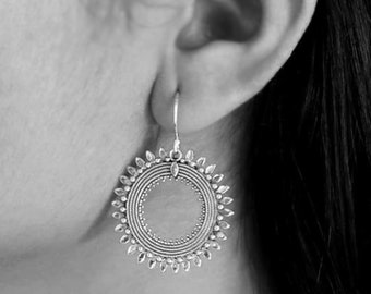 Può includere: Orecchini pendenti in argento con un design circolare che presenta più cerchi concentrici e un bordo decorativo di piccole foglie.
