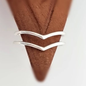 Può includere: Due anelli a chevron argentati impilati uno sopra l'altro. Gli anelli sono sottili e delicati, e sono realizzati in un metallo liscio e lucido.