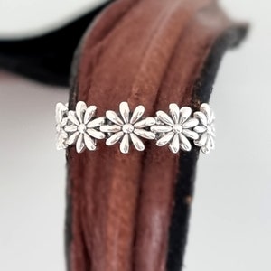 Könnte beinhalten: Ein silberner Ring mit einem Gänseblümchen-Design. Der Ring besteht aus fünf Gänseblümchen, die miteinander verbunden sind.