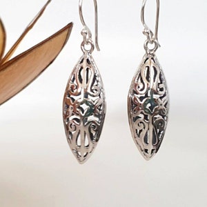 May include: A pair of silver filigree earrings with a delicate, intricate design. The earrings are shaped like a teardrop and have a dangling drop.