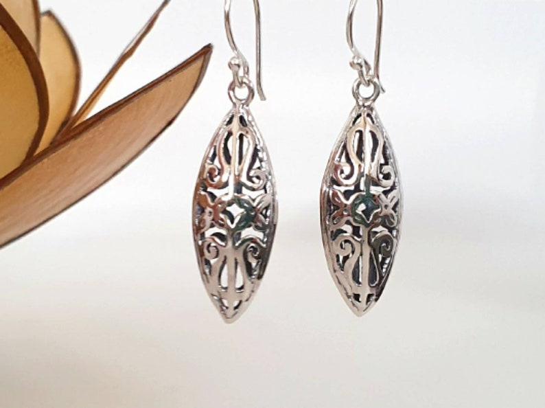 May include: A pair of silver filigree earrings with a delicate, intricate design. The earrings are shaped like a teardrop and have a dangling drop.