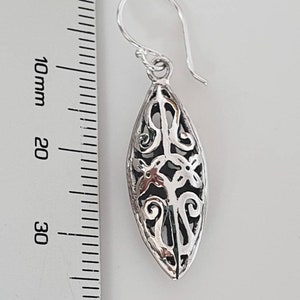 May include: Silver filigree dangle earrings with a teardrop shape. The earrings are approximately 3.5 cm long.
