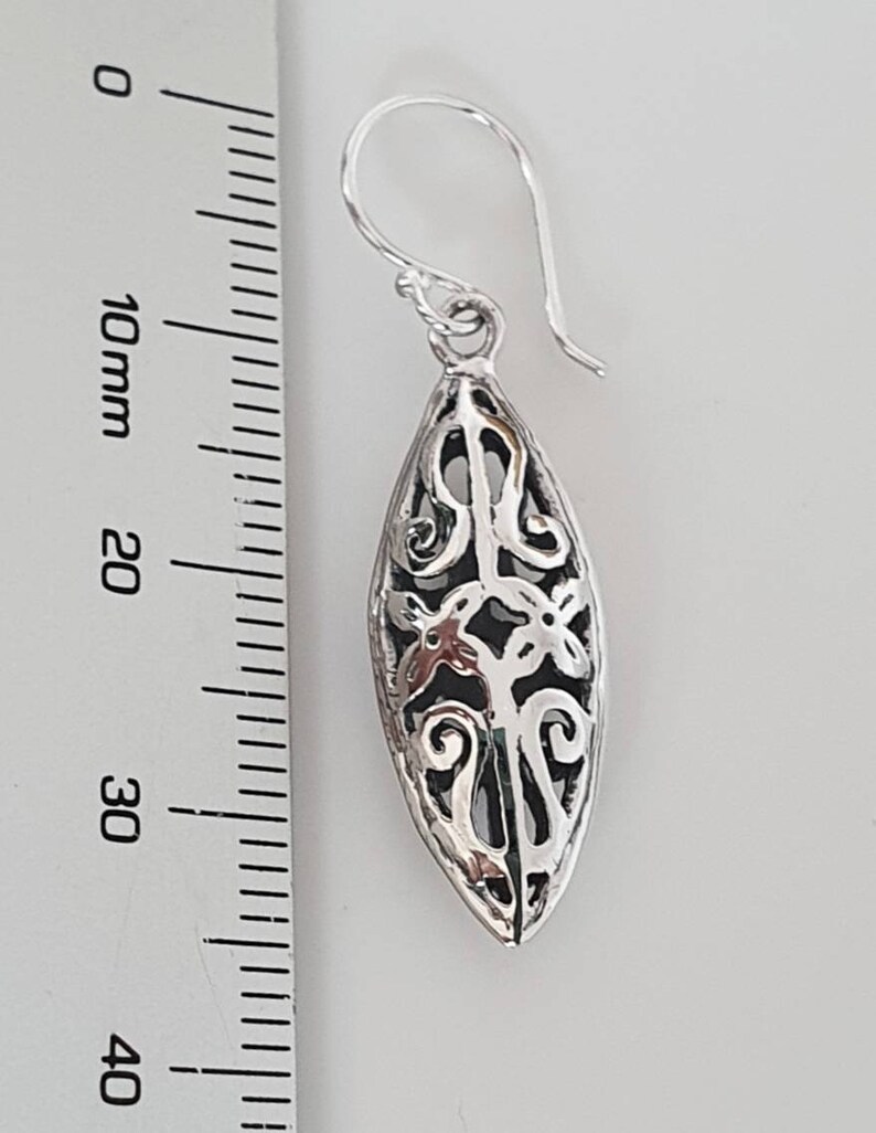 May include: Silver filigree dangle earrings with a teardrop shape. The earrings are approximately 3.5 cm long.