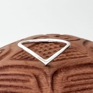 Op de afbeelding: Een eenvoudige zilveren ring met een V-vormig ontwerp. De ring wordt getoond op een houten oppervlak.