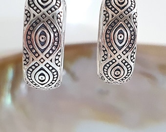May include: A pair of silver hoop earrings with a geometric pattern. The pattern features a repeating design of circles and ovals.
