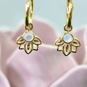 Peut inclure: Boucles d'oreilles créoles dorées avec un délicat motif de fleur de lotus et un centre blanc nacré.