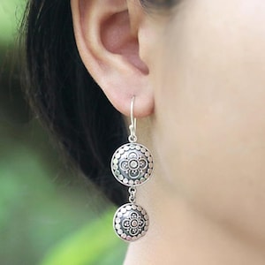 May include: Silver dangle earrings with two round discs. Each disc has a floral design with a raised center.
