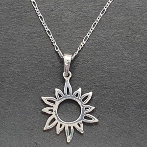 Könnte beinhalten: Eine silberne Halskette mit einem Sonnenanhänger. Der Anhänger ist ein einfacher, offener Kreis mit Strahlen, die von ihm ausgehen.