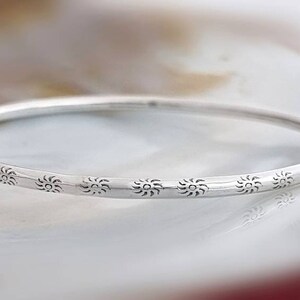 Peut inclure: Un bracelet jonc en argent avec un délicat motif de soleil gravé autour de la bande.